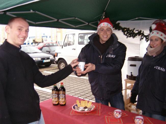 Promoter am Glühweinstand überreichen einem Besucher warmen Glühwein.