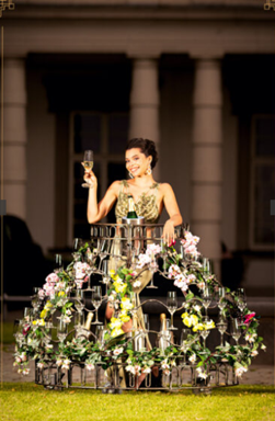 Künstlerin Leony La Roc im Champagnerkleid Deluxe, geschmückt mit Blumen und Sektgläsern, für einen exklusiven Sektempfang bei einem Event.