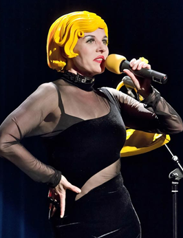 Comedienne Bartuschka in einem roten Overall und gelbem Bauhelm begeistert das Publikum mit einer rasanten Comedy-Show auf der Bühne.